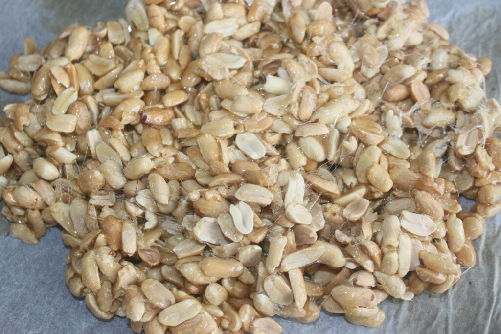 Gros plan de nombreux cacahuètes crus avec peau, empilés sur un morceau de papier sulfurisé.