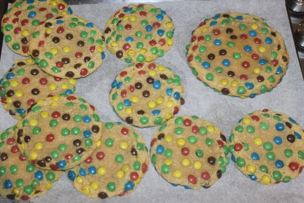 Un lot de biscuits garnis de mini M&M's aux couleurs vives repose sur une plaque à pâtisserie recouverte de papier sulfurisé.