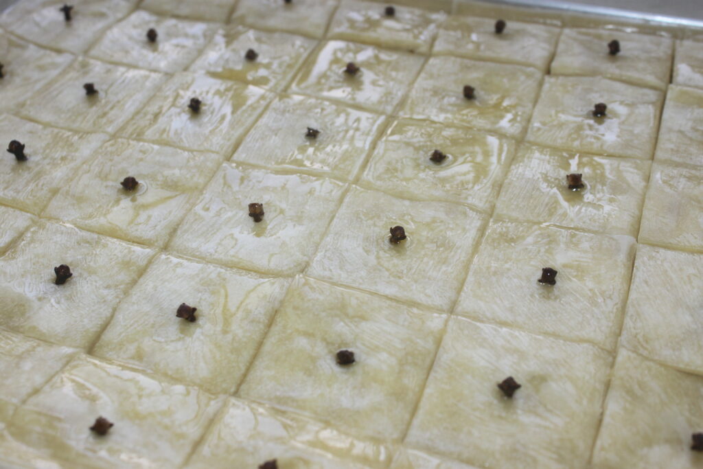 Un plateau de baklava cru est divisé en sections carrées, chacune surmontée d'un clou de girofle et remplie d'un riche mélange de noix finement hachées, rendant hommage à ses origines grecques.