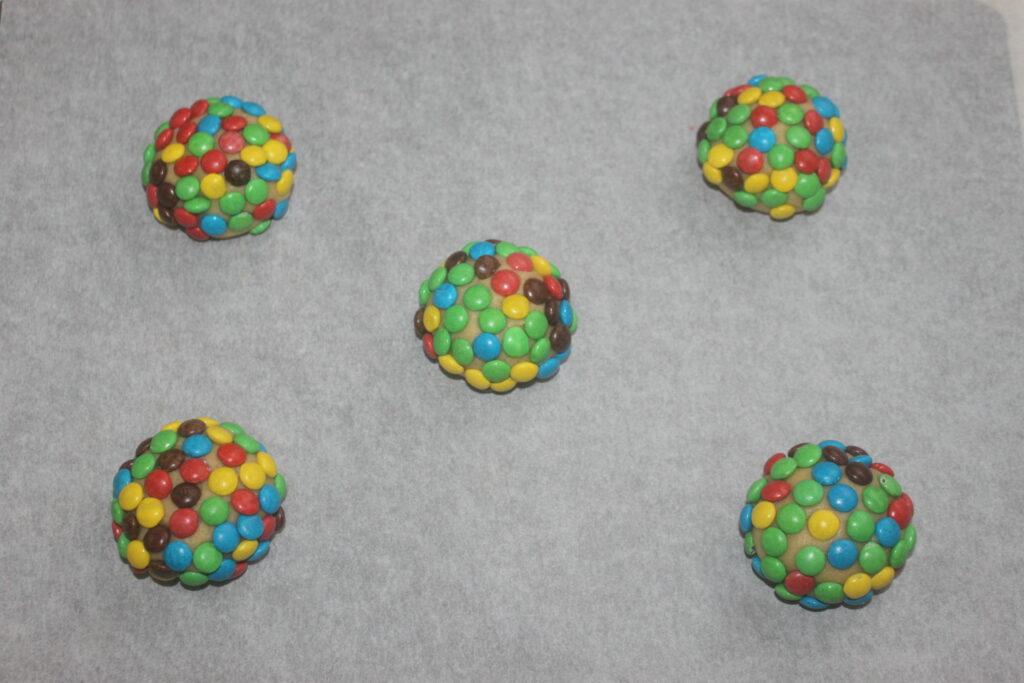 Cinq biscuits ronds parsemés de mini M&M's, chacun d'une délicieuse explosion de couleurs, reposent de manière invitante sur une plaque à pâtisserie.