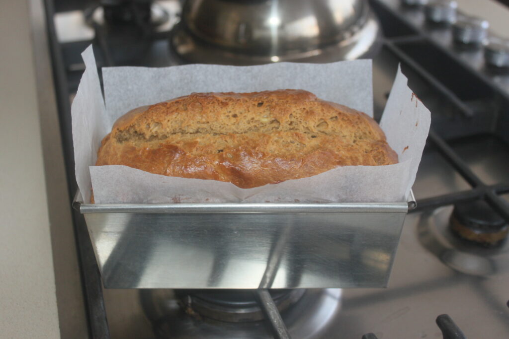 Un pain de banane dans un moule en métal recouvert de papier sulfurisé est posé sur la cuisinière, fraîchement cuit et légèrement doré sur le dessus.