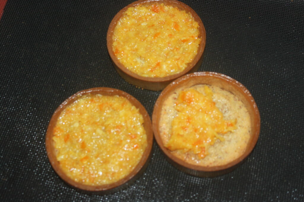 Trois Tartelettes à la crème d'orange reposent sur une surface noire, présentant un délice de dessert sucré.