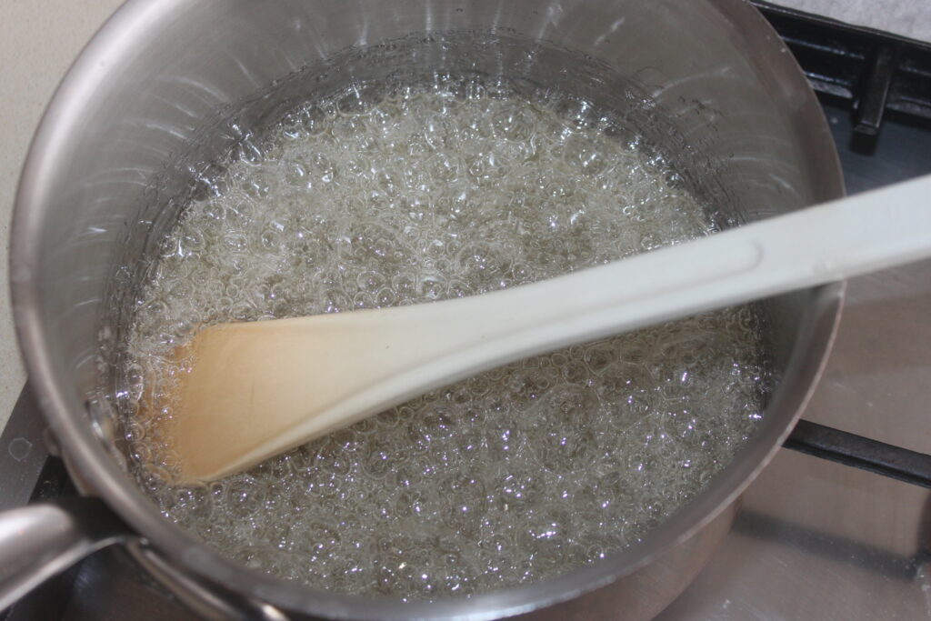 Une casserole de sirop de sucre bout sur une cuisinière, prête à être transformée en une délicieuse garniture de tarte, avec une cuillère en bois posée à l'intérieur.
