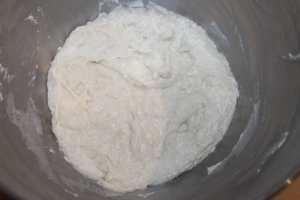 Un bol contenant une pâte blanche et collante, peut être pour du pain ou de la pizza, est niché dans un saladier en métal. À côté de la pâte qui lève, on pourrait imaginer l'arôme savoureux des galettes de shitakés ou de tofu qui attendent leur tour au four.