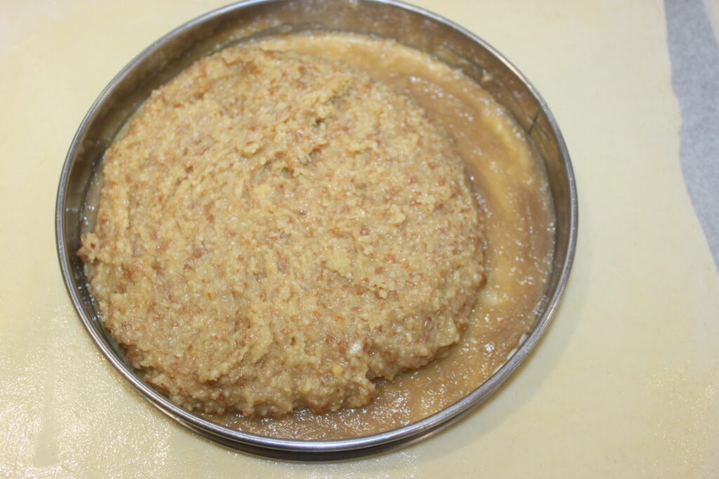 Un moule à gâteau rond rempli d'un mélange épais, beige, semblable à une pâte infusée de caramel, repose sur une surface de couleur claire.