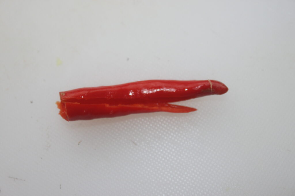Un seul piment rouge, coupé en deux et posé sur un fond blanc, évoque l'épice vibrante qui se marie parfaitement avec les shitakés ou le tofu dans vos plats préférés.