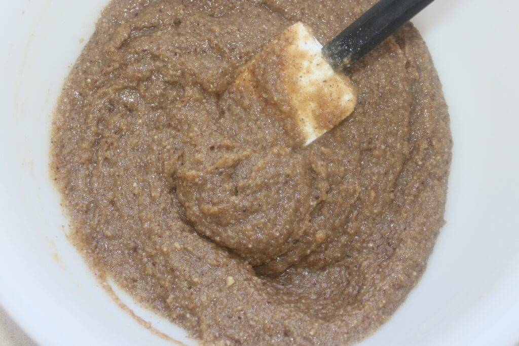 Une pâte brune, riche en arôme de noisette, est mélangée à la spatule dans un bol blanc.
