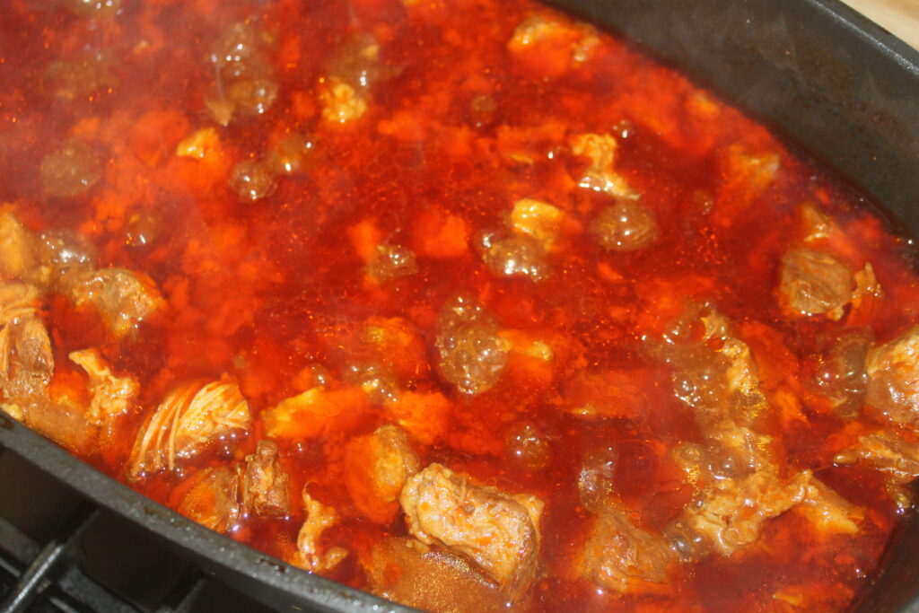 Gros plan d'un riche ragoût rouge avec des morceaux de viande mijotant dans une grande casserole.