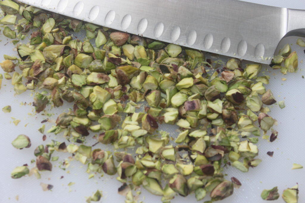 Pistaches hachées sur une planche à découper avec un couteau posé à côté d'elles, prêtes à ajouter une touche croustillante à votre feta croustillante au miel.