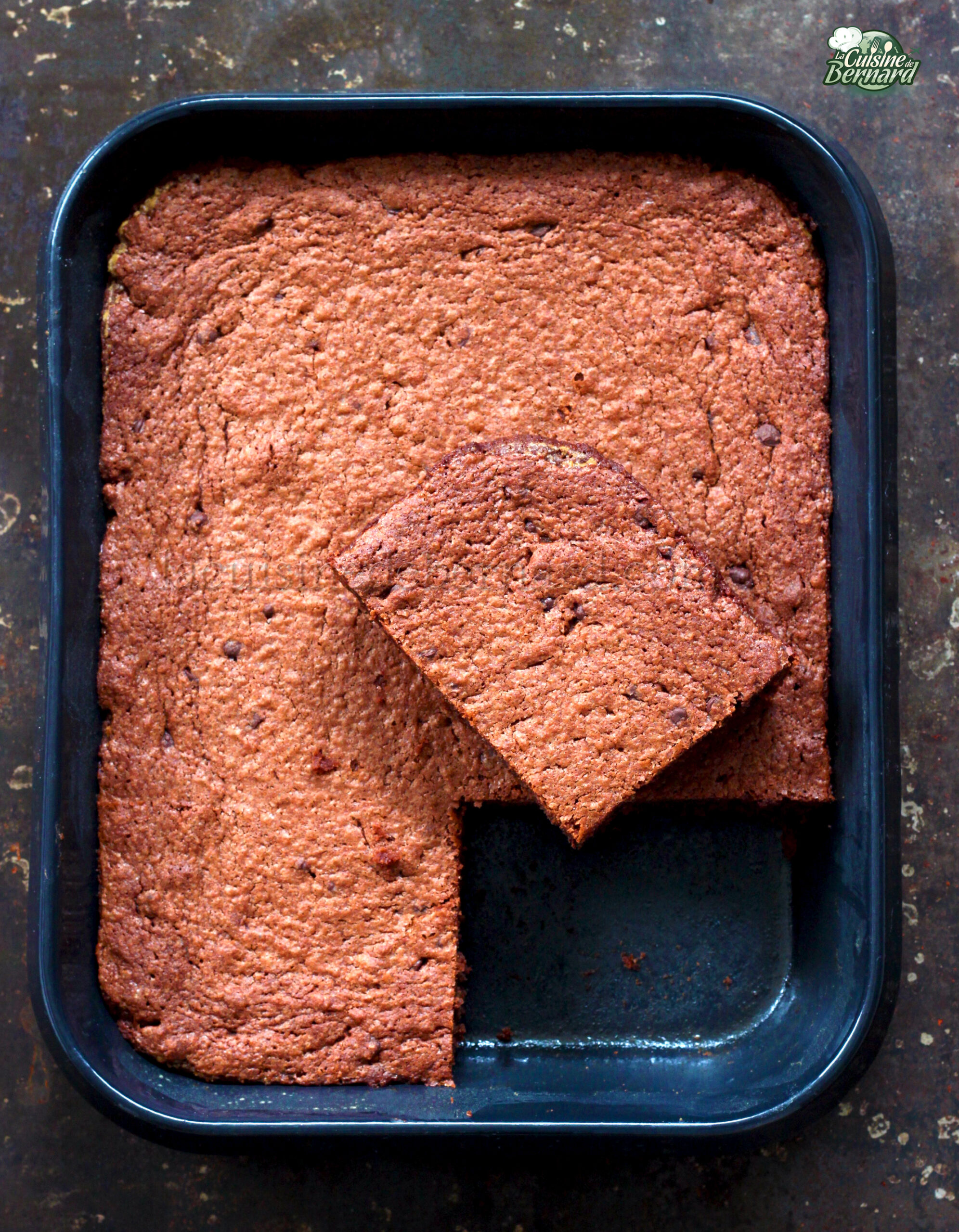 Un plateau de brownies riches en chocolat gâteau avec un morceau carré découpé et légèrement surélevé au dessus du reste, révélant des pépites de chocolat éparpillées.