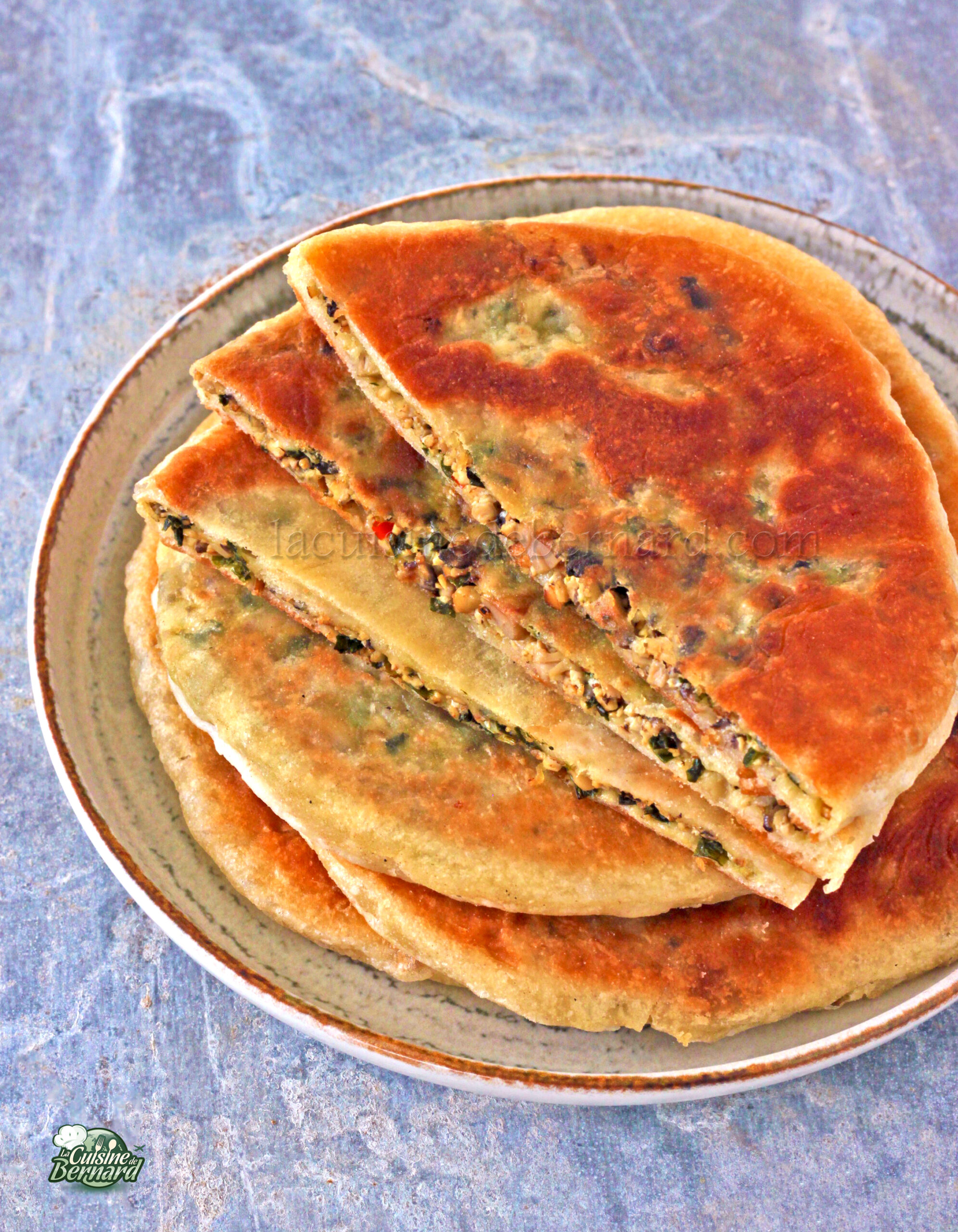 Une assiette avec quatre morceaux de pain plat farcis, empilés et légèrement superposés, présentant une garniture de tofu, d'herbes et de légumes.